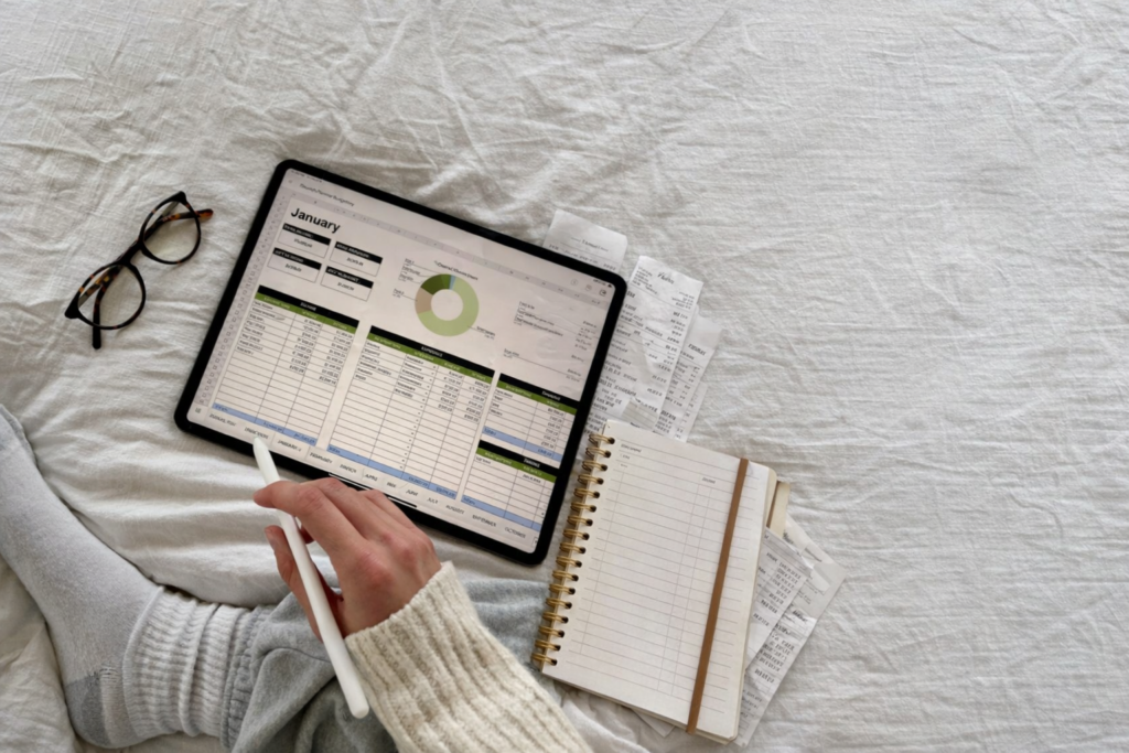 A cozy budgeting setup on a bed with a tablet displaying a financial spreadsheet, a weekly planner, receipts, and a stylus , part of an organized Sunday reset routine.