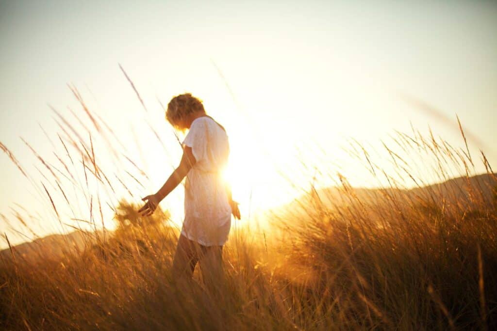 Person standing in tall golden grass during sunset, softly lit by warm natural light, creating a peaceful and nature‑connected atmosphere.