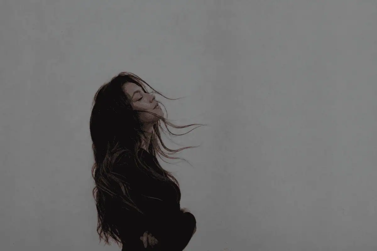 Moody minimalist portrait of a young woman with windblown dark hair standing against a soft grey background, symbolizing healing, anxiety recovery, and emotional resilience.