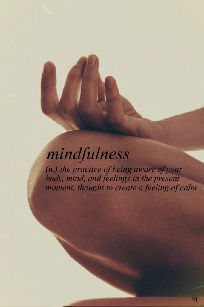 A close-up of a hand resting on a bent knee in a meditative pose, with soft lighting and text defining mindfulness as being present in body and mind.