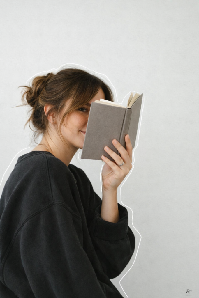 Woman playfully hiding behind a gray book, minimalist reading moment with cozy vibes.