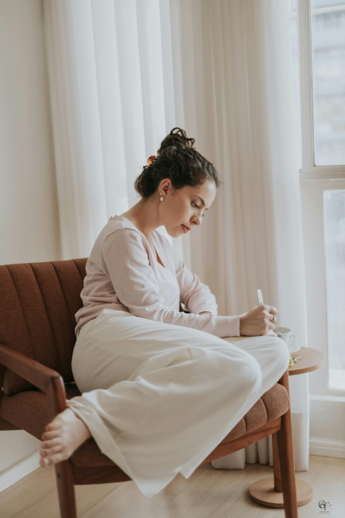 Woman sitting barefoot by a window writing in a journal with tea beside her, soft natural light
Journal Prompts for Overthinking